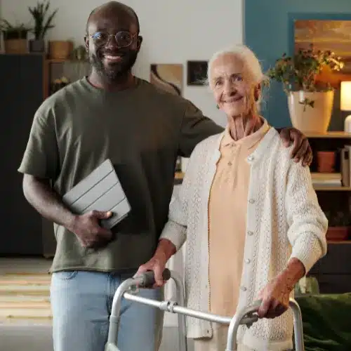 Caregiver standing with a smiling senior woman using a walker at home